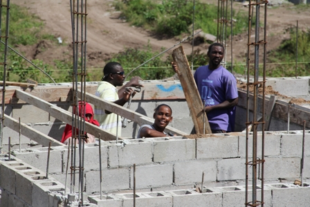 The sole female looks to the camera, hammer in hand, at work with her male colleagues on the construction site at the Nevis Housing and Lands Development Corporation Colquhoun Housing Development at Jessups Village